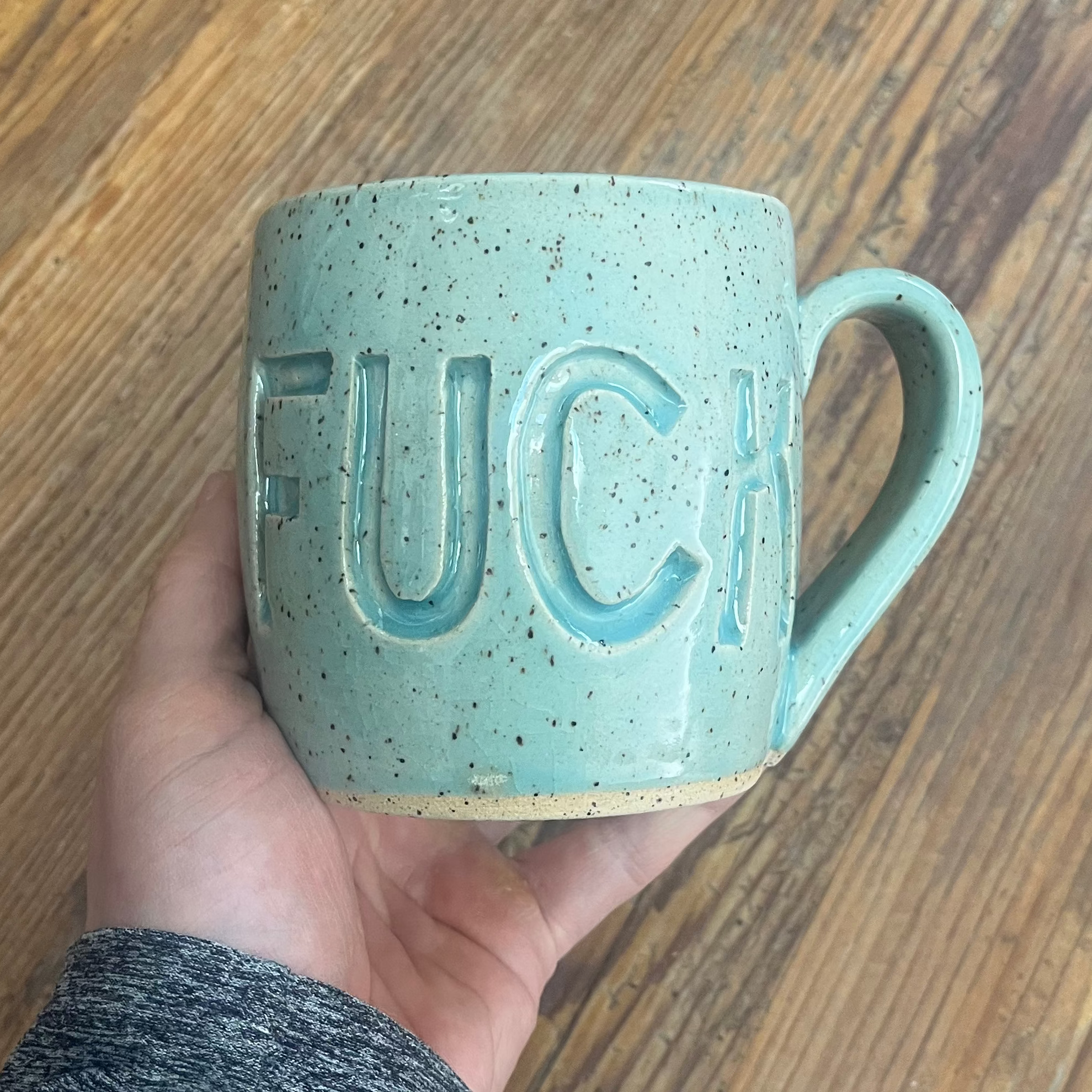 Hand holding an aqua mug with fuck carved into it.