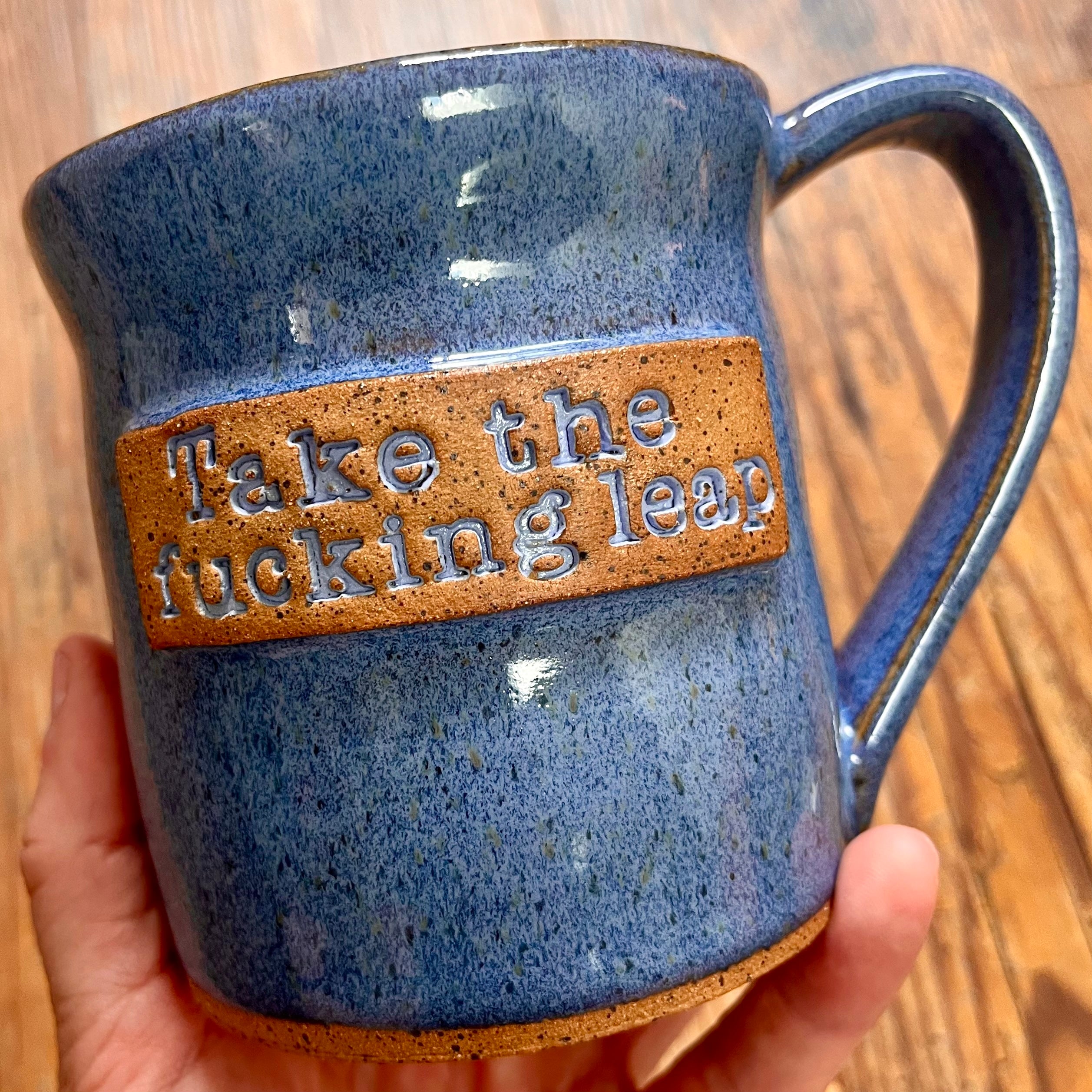 A blue  mug featuring the phrase "Take the fucking leap"