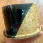 A planter with one half glazed in metallic black and one half glazed in clear