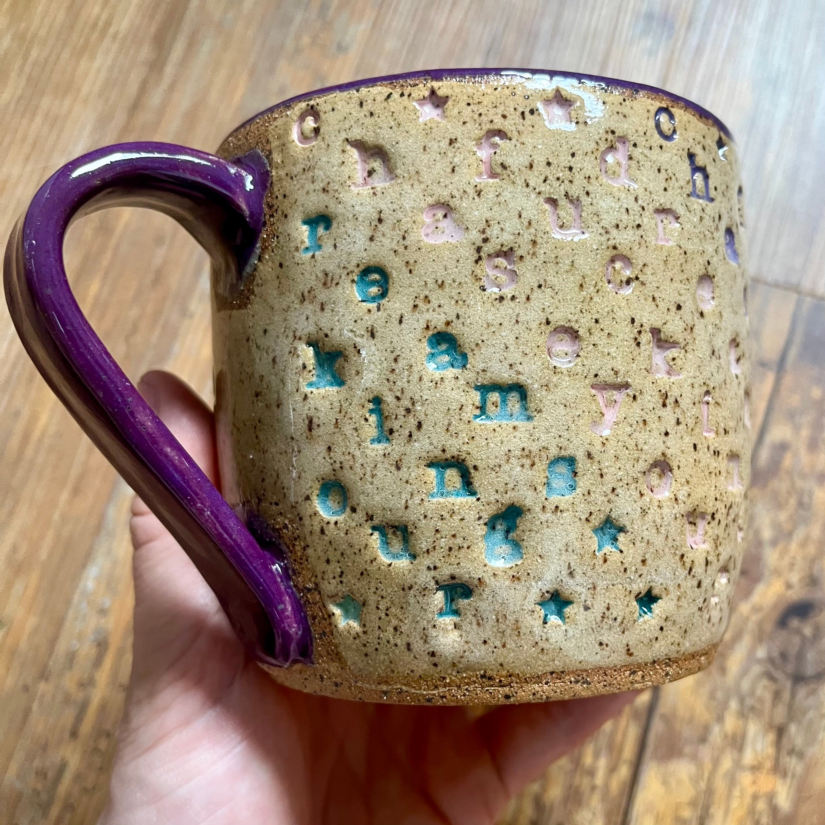 a mug with "chase your fucking dreams" stamped in diagonal stripes with a purple handle