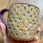 a mug with "chase your fucking dreams" stamped in diagonal stripes with a purple handle