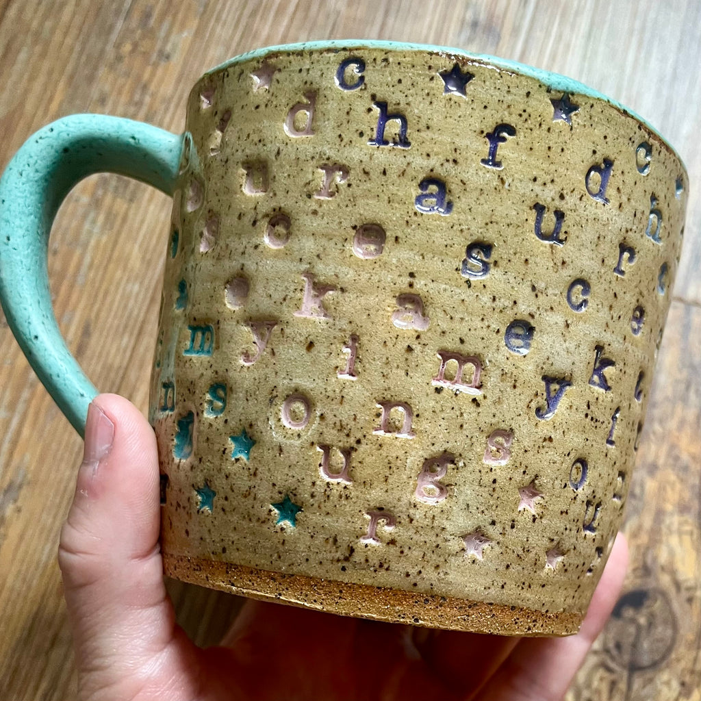 a mug with "chase your fucking dreams" stamped in diagonal stripes with a seaglass colored handle