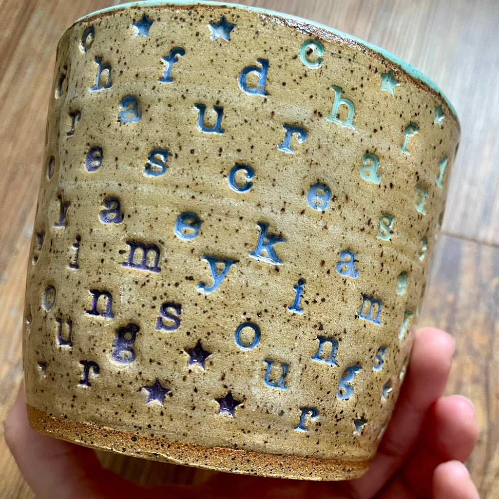 a mug with "chase your fucking dreams" stamped in diagonal stripes with a seaglass colored handle