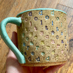 A mug with "do it scared" stamped in diagonal rainbow-colored stripes with a seaglass colored handle