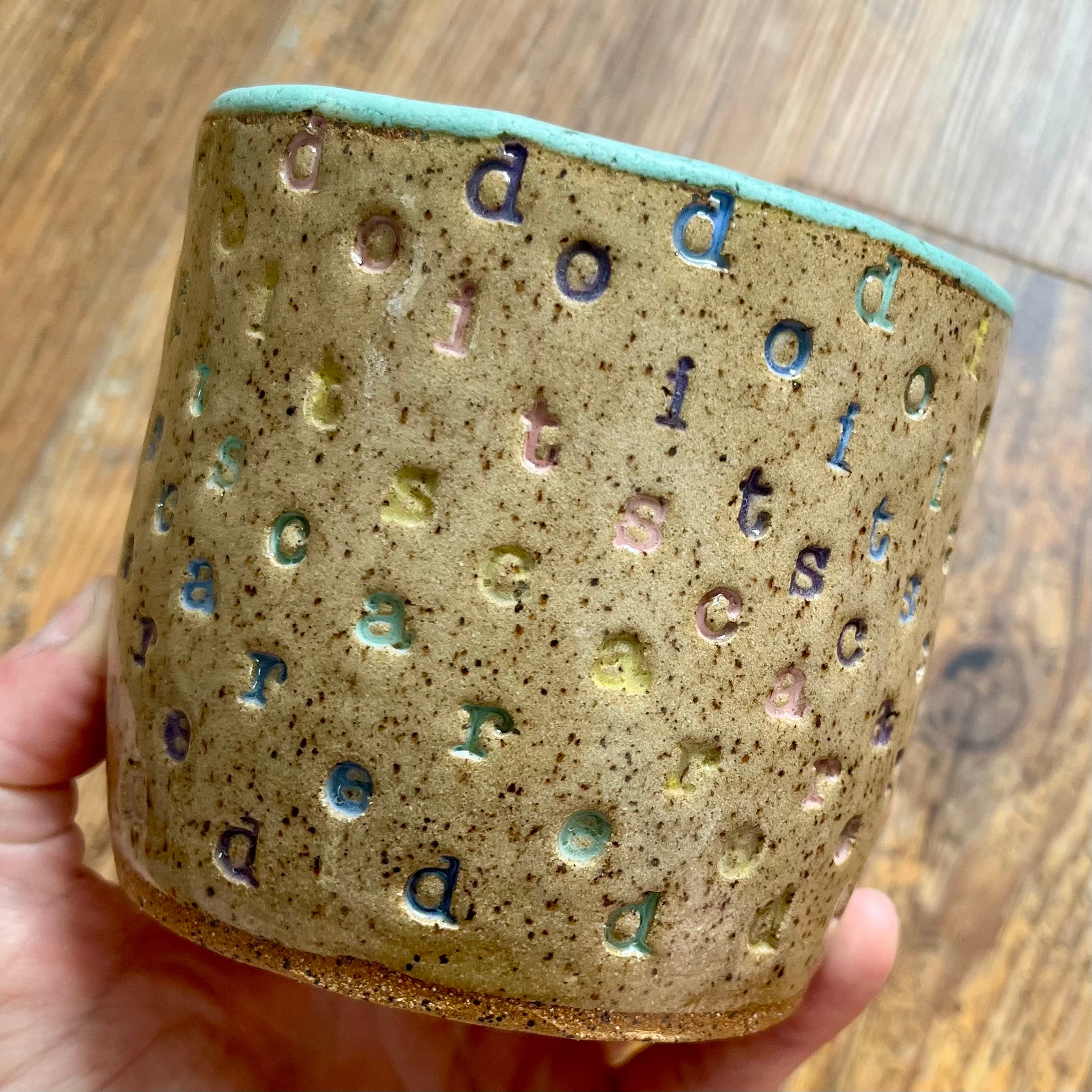 A mug with "do it scared" stamped in diagonal rainbow-colored stripes with a seaglass colored handle