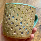 A mug with "do it scared" stamped in diagonal rainbow-colored stripes with a seaglass colored handle