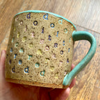 A mug with "do it scared" stamped in diagonal rainbow-colored stripes with a seaglass colored handle