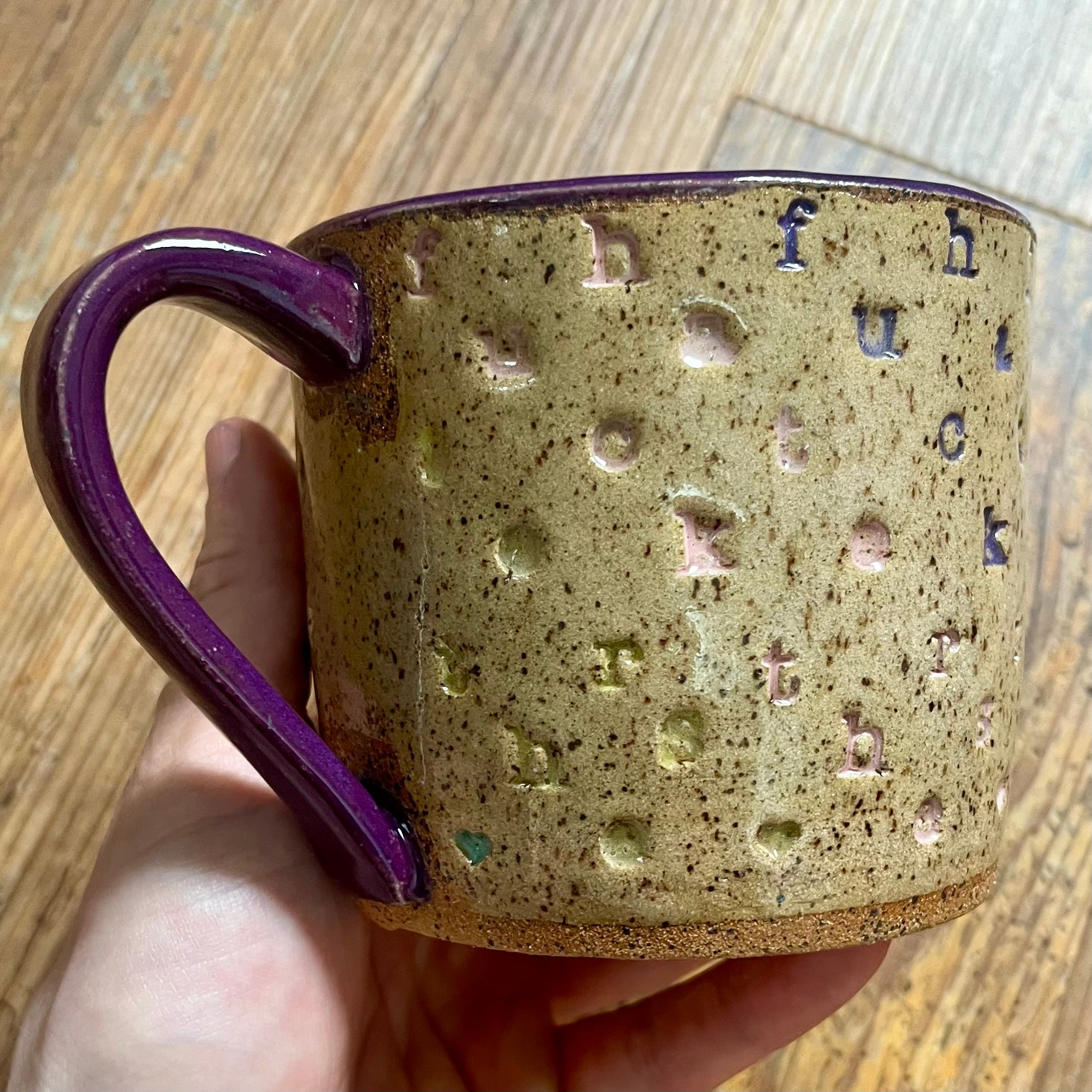 a mug with f*ck the haters stamped in diagonal stripes with a purple handle