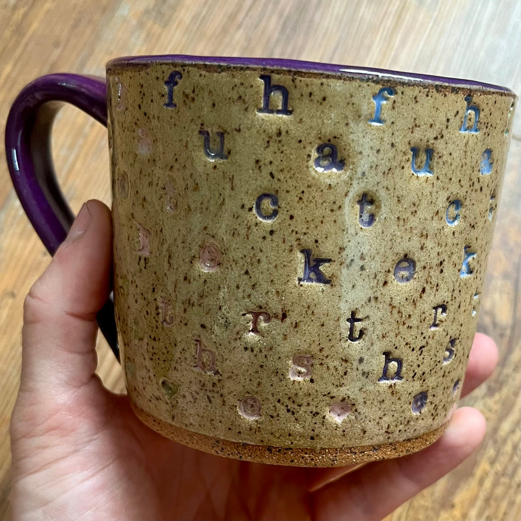 a mug with f*ck the haters stamped in diagonal stripes with a purple handle
