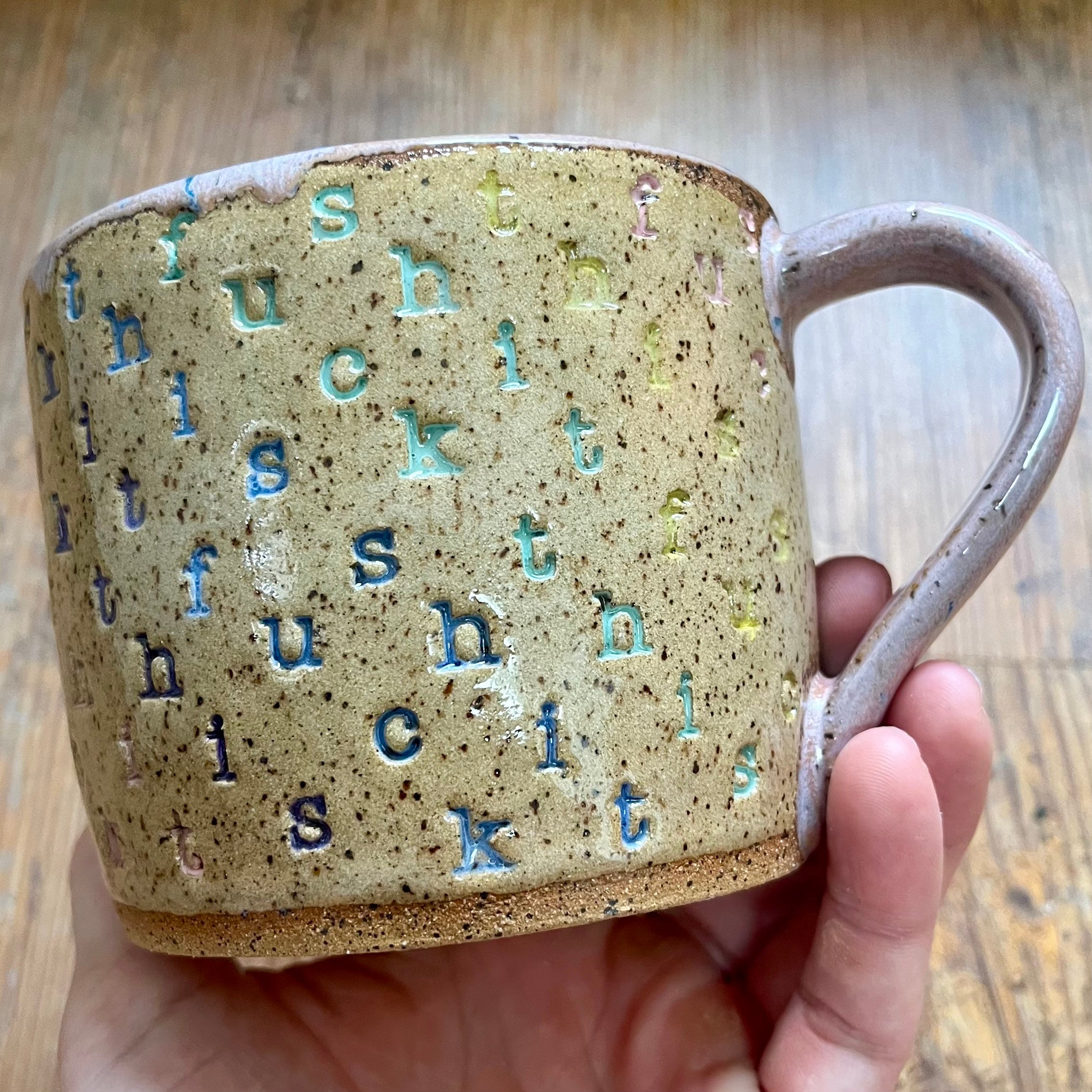 A mug with "f*ck this sh*t stamped in diagonal stripes in a rainbow of colors
