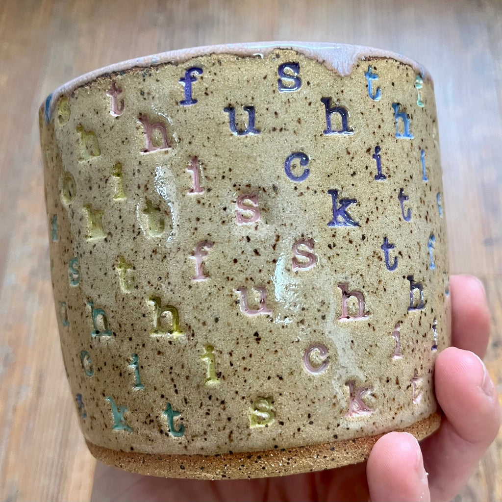 A mug with "f*ck this sh*t stamped in diagonal stripes in a rainbow of colors