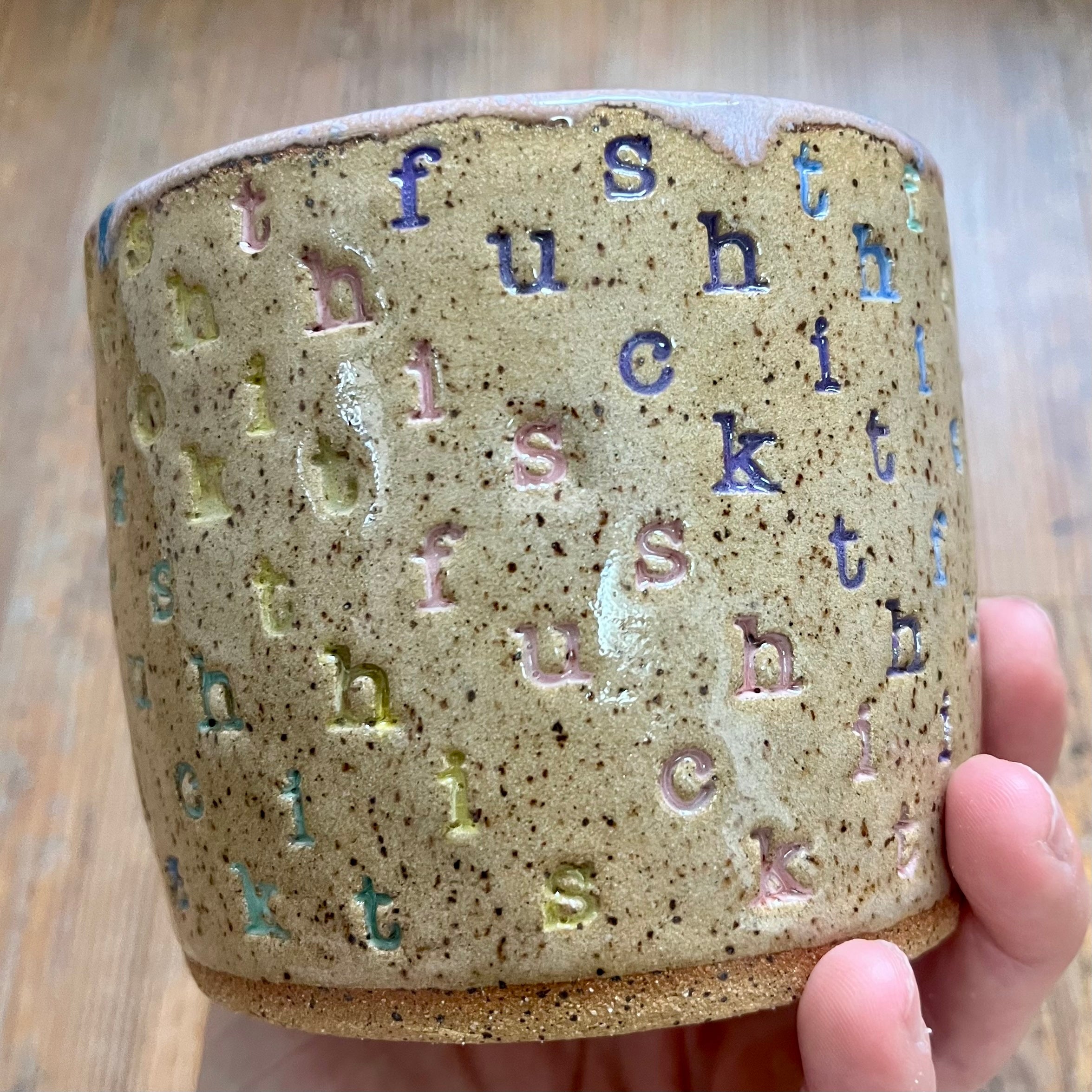 A mug with "f*ck this sh*t stamped in diagonal stripes in a rainbow of colors