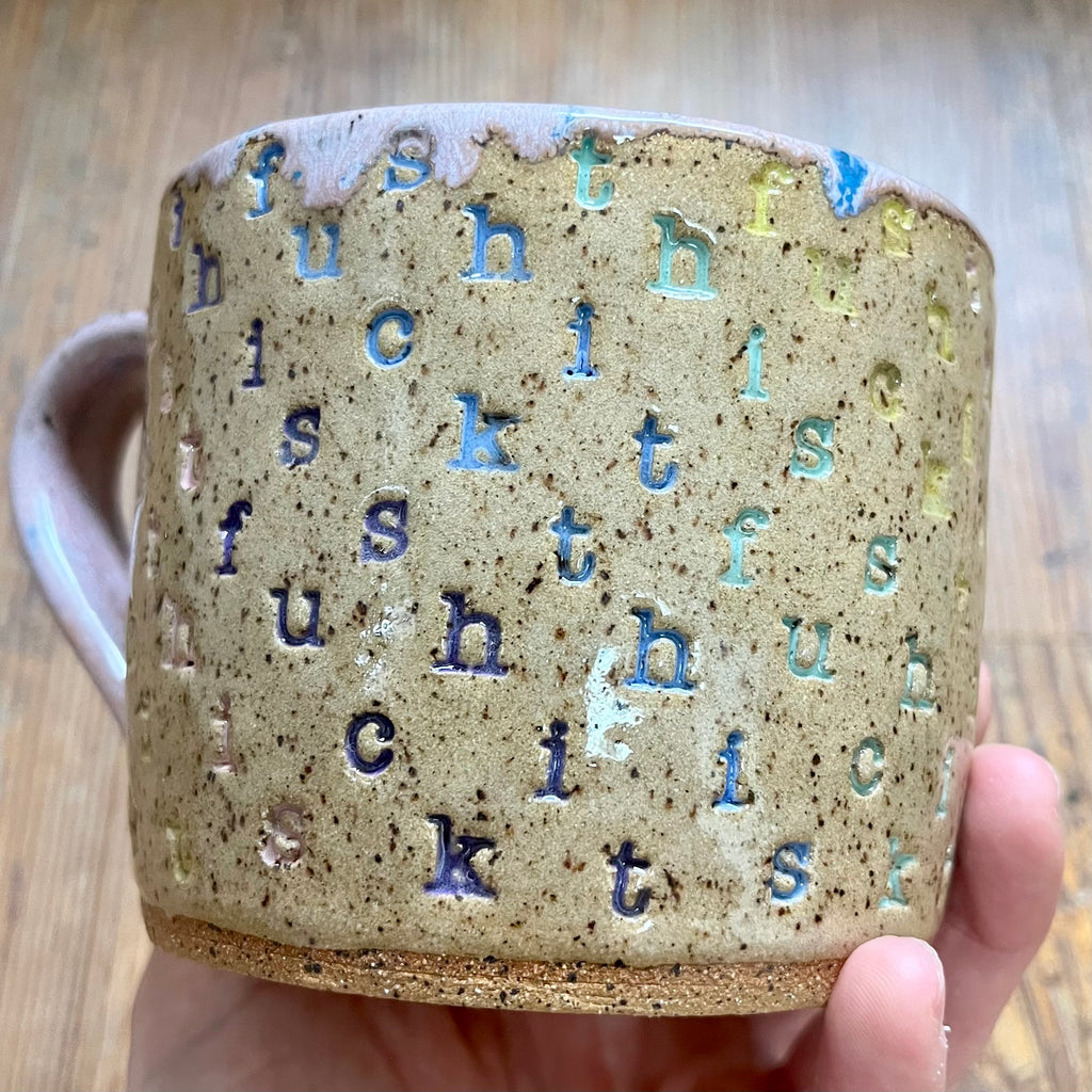 A mug with "f*ck this sh*t stamped in diagonal stripes in a rainbow of colors