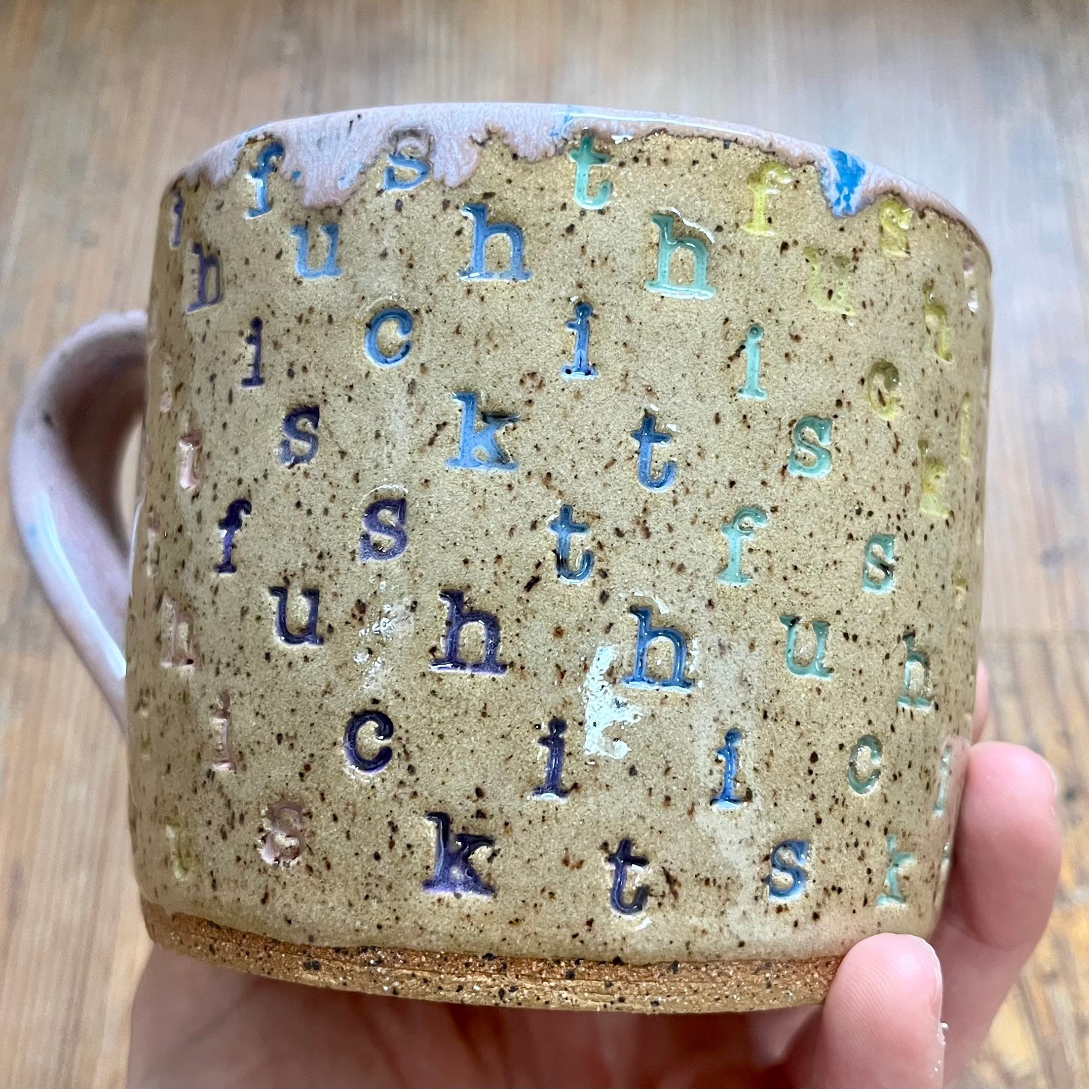 A mug with "f*ck this sh*t stamped in diagonal stripes in a rainbow of colors