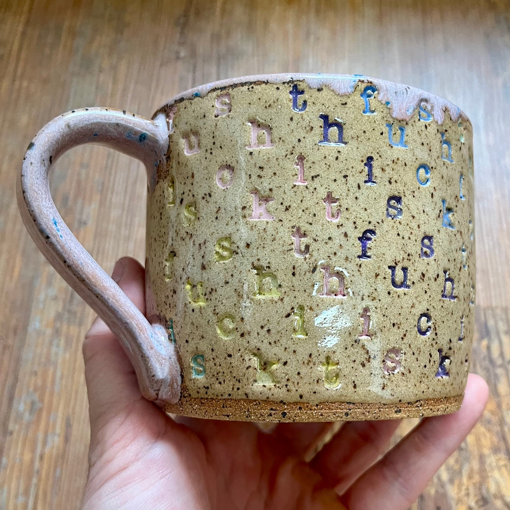 A mug with "f*ck this sh*t stamped in diagonal stripes in a rainbow of colors