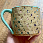 A mug stamped with "f*ck this sh*t" in diagonal stripes with a seaglass colored handle