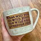 A white mug with purple texting reading "What will you do with your one wild and precious life?"