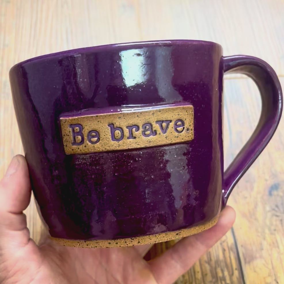A video rotating around a purple mug with the phrase "be brave" on it
