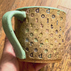 a video rotating around a mug with "do it scared" stamped in diagonal rainbow-colored stripes with a seaglass colored handle