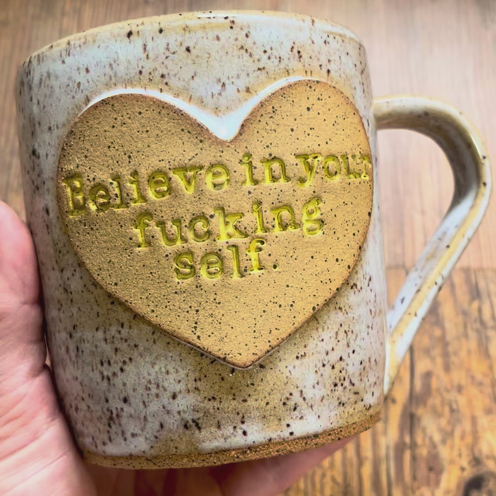 A video rotating around a white mug featuring the phrase "Believe in your fucking self" in a clay heart