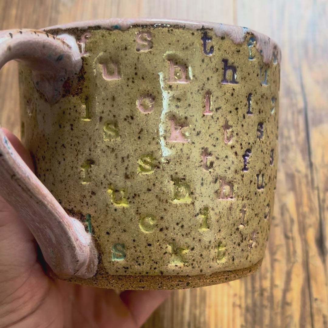 A video rotating around a mug with "f*ck this sh*t stamped in diagonal stripes in a rainbow of colors