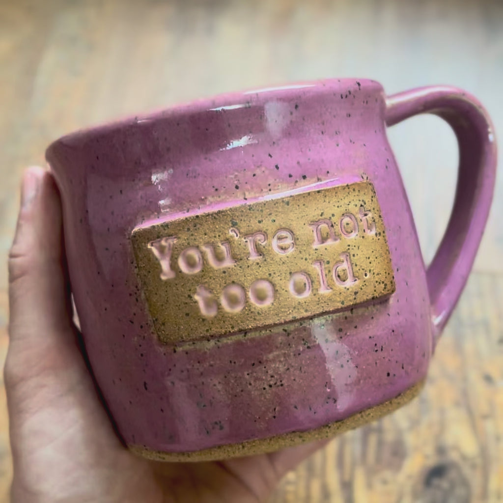 A video rotating around a pink mug featuring the phrase "you're not too old"