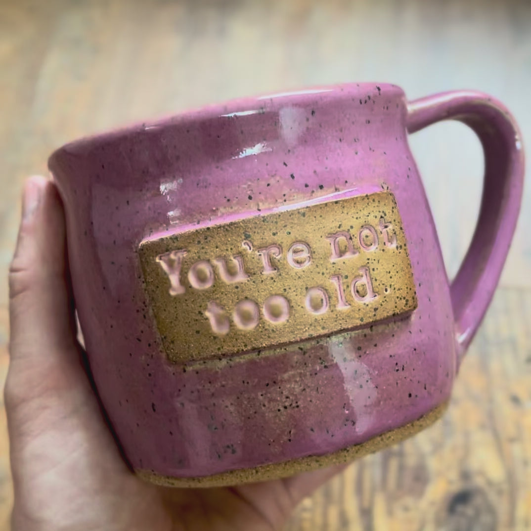A video rotating around a pink mug featuring the phrase "you're not too old"