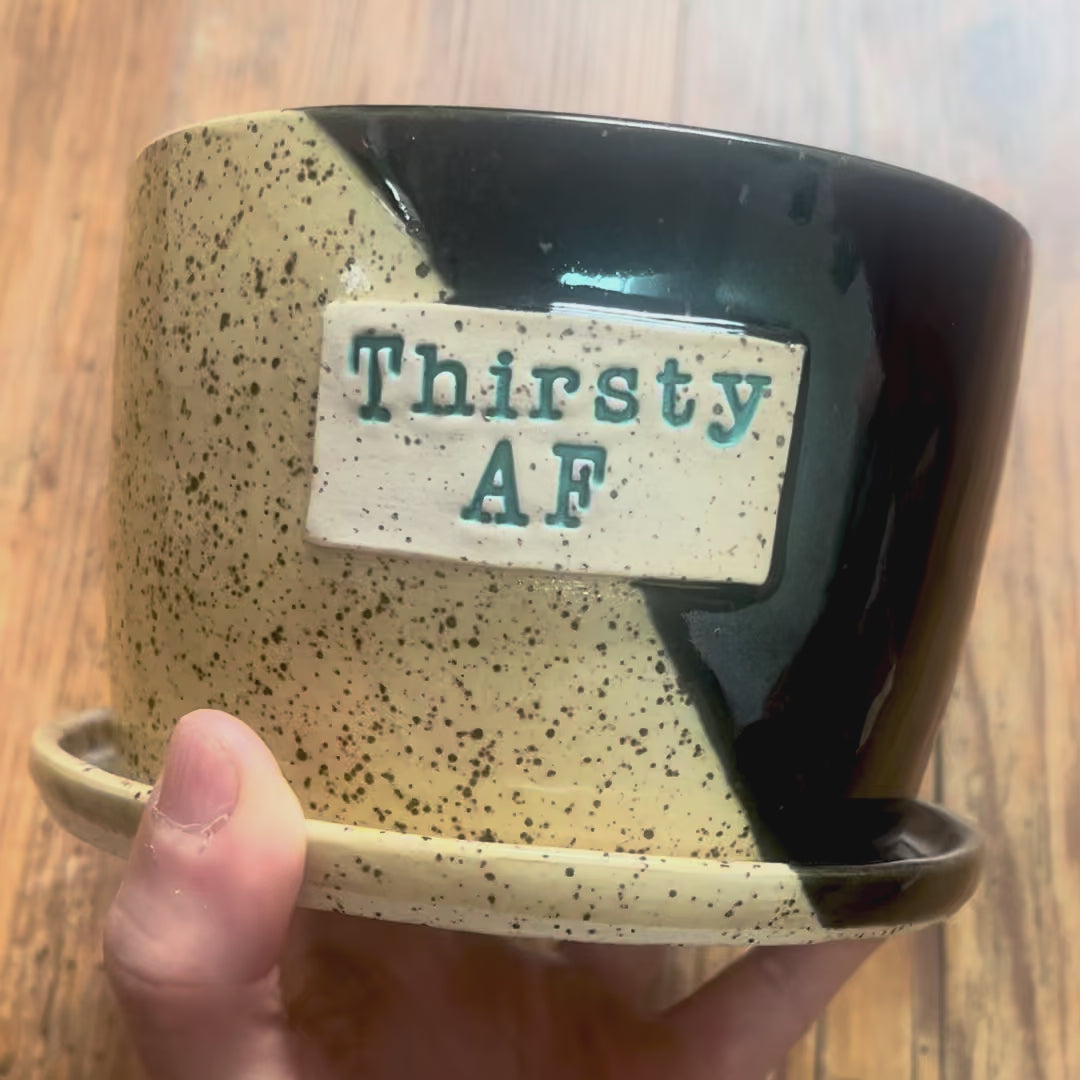 A video showing a planter glazed in metallic black and clear glaze with the phrase Thirsty AF on a rectangular patch of clay.