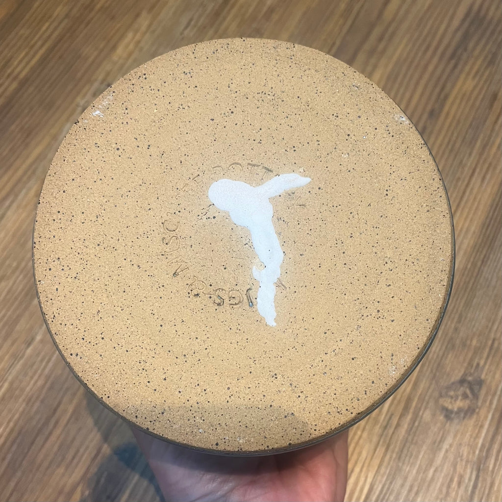 the bottom of a handmade ceramic planter, showing a repaired crack, held by a hand over a wooden table.