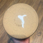 the bottom of a handmade ceramic planter, showing a repaired crack, held by a hand over a wooden table.